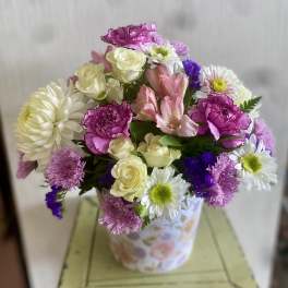 Mixed bouquet of pink, white, and purple flowers in a floral paper container