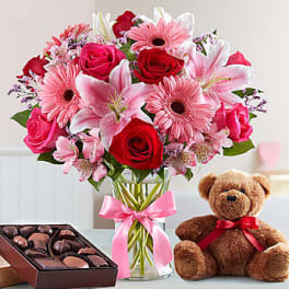 Pink and red mixed bouquet in a glass vase with a teddy bear and chocolates