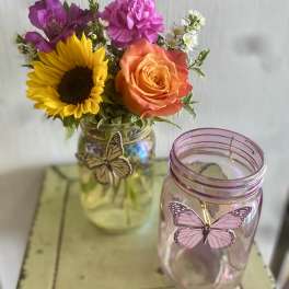 Mixed bouquet in a glass jar beside a pink butterfly jar candle