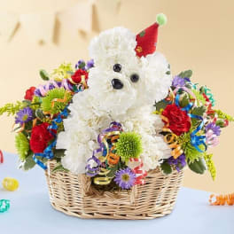 White teddy bear in a basket surrounded by colorful flowers and ribbons