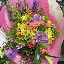 Mixed bouquet of pink roses, yellow daisies, and purple flowers wrapped in pink paper