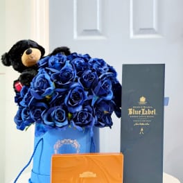 Blue rose bouquet in a gift box with a teddy bear, whiskey box, and chocolates