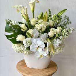 White floral arrangement in a white vase with calla lilies, roses, and orchids