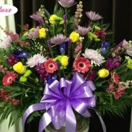 Large mixed flower arrangement with a purple ribbon bow