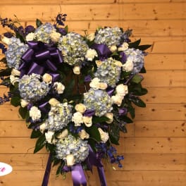 Heart-shaped floral wreath with blue hydrangeas, white roses, and purple ribbon