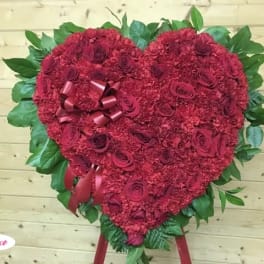 Heart-shaped red floral arrangement with ribbon accents and green leaves