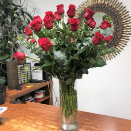 Tall vase of red roses with eucalyptus on a desk