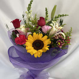 Mixed bouquet with a sunflower, roses, lilies, and purple wrapping