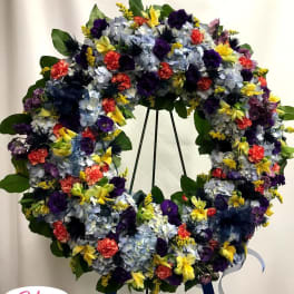 Large floral wreath on a stand with blue, purple, yellow, and coral flowers