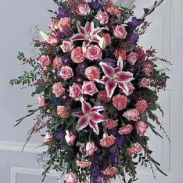 Tall standing floral spray with pink roses and lilies in pink, purple, and white.