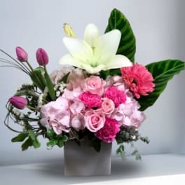 Pink floral arrangement with a white lily in a square vase