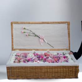 Open wicker casket filled with pink and white flowers and two pink carnations on the lid.