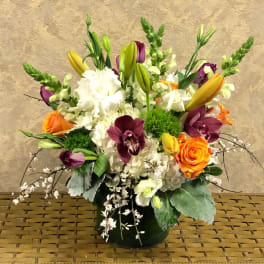Mixed bouquet with orange roses, purple orchids, white blooms, and lilies in a vase