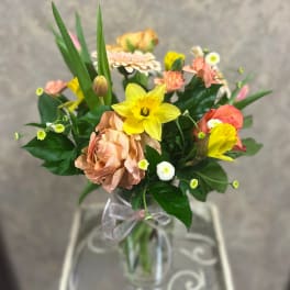 Mixed bouquet with yellow daffodils, peach roses, and small white daisies in a glass vase