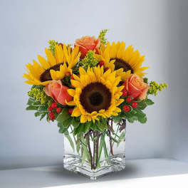 Sunflowers and peach roses arranged in a clear glass vase