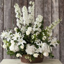 White floral arrangement in a wicker basket with lilies and roses