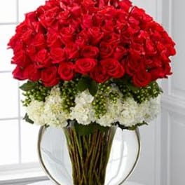 Large arrangement of red roses over white flowers in a round clear glass vase