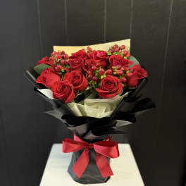 Bouquet of red roses with berry accents wrapped in black paper and a red ribbon
