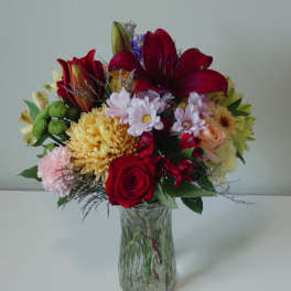 Mixed bouquet of red, pink, yellow, and purple flowers in a clear glass vase