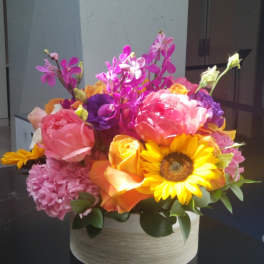 Bright mixed bouquet in a round box with sunflowers, roses, and orchids