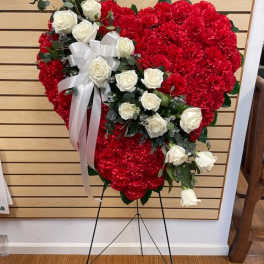Heart-shaped red carnation wreath with white roses and a white ribbon on an easel
