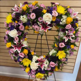 Heart-shaped floral wreath on a stand with pink, white, yellow, and purple flowers