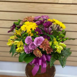 Mixed bouquet of purple, yellow, and pink flowers in a vase with a ribbon