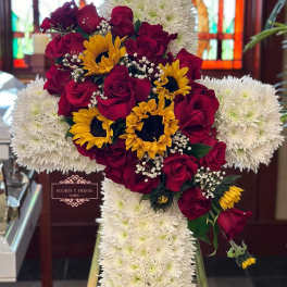 Cross-shaped floral arrangement with red roses, yellow sunflowers, and white chrysanthemums