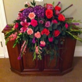 Large mixed floral arrangement with red roses and purple blooms in a wooden casket spray