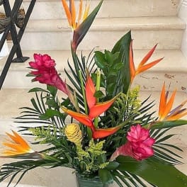 Tall tropical arrangement with orange and pink flowers and lush foliage in a low rectangular container
