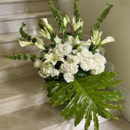 Large white arrangement with lilies, roses, and a big green tropical leaf on marble steps