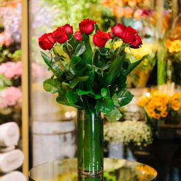 Red roses arranged in a tall green glass vase