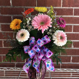 Colorful gerbera daisy arrangement in a purple vase with a patterned bow