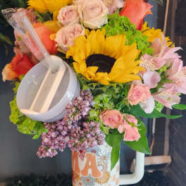 Bright mixed bouquet with sunflowers and roses arranged in a tall patterned travel mug with lid and straw.