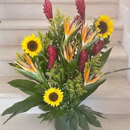 Tall tropical arrangement with yellow sunflowers and orange bird-of-paradise in a glass vase