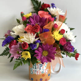 Colorful mixed flower bouquet in a birthday mug with orange ribbon