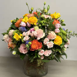 Colorful arrangement of pink roses and mixed bright blooms in a ribbed glass cylinder vase