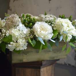 White floral arrangement in a wooden box with greenery