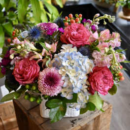 Colorful arrangement of pink roses, mums, and blue hydrangeas in a white vase