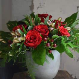 Red roses arranged in a white vase with green foliage and berry accents