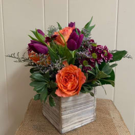 Orange roses and purple tulips in a square wooden vase