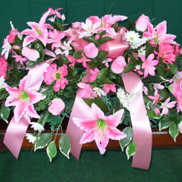 Pink floral casket spray with lilies and roses on a dark surface