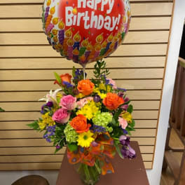Birthday balloon above a colorful mixed flower arrangement in a glass vase