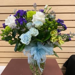 Bouquet of white and pale blue roses with purple filler in a glass vase