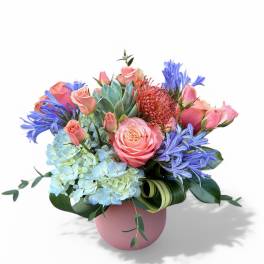 Pink roses and blue flowers arranged in a pink vase