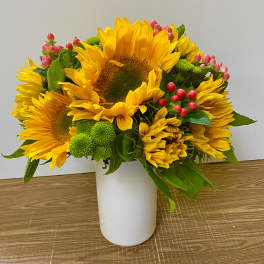 Sunflower bouquet in a white vase with pink berries and green button mums