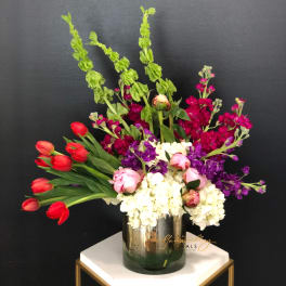 Mixed bouquet of red tulips, white hydrangeas, and purple flowers in a glass vase