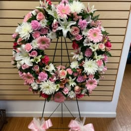 Pink and white floral wreath on a black stand with pink bows