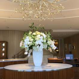 Large white floral arrangement in a tall vase on a lobby table