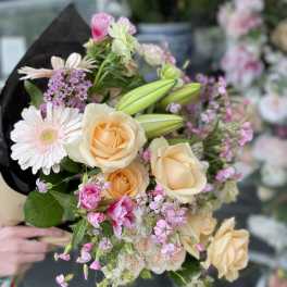 Bouquet of peach roses, pink daisies, and lilies wrapped in dark paper